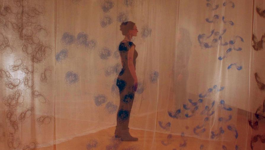 a woman standing looking off to the right in the distance, while it looks like the viewer is looking through brownish, blue detailed lace tarp