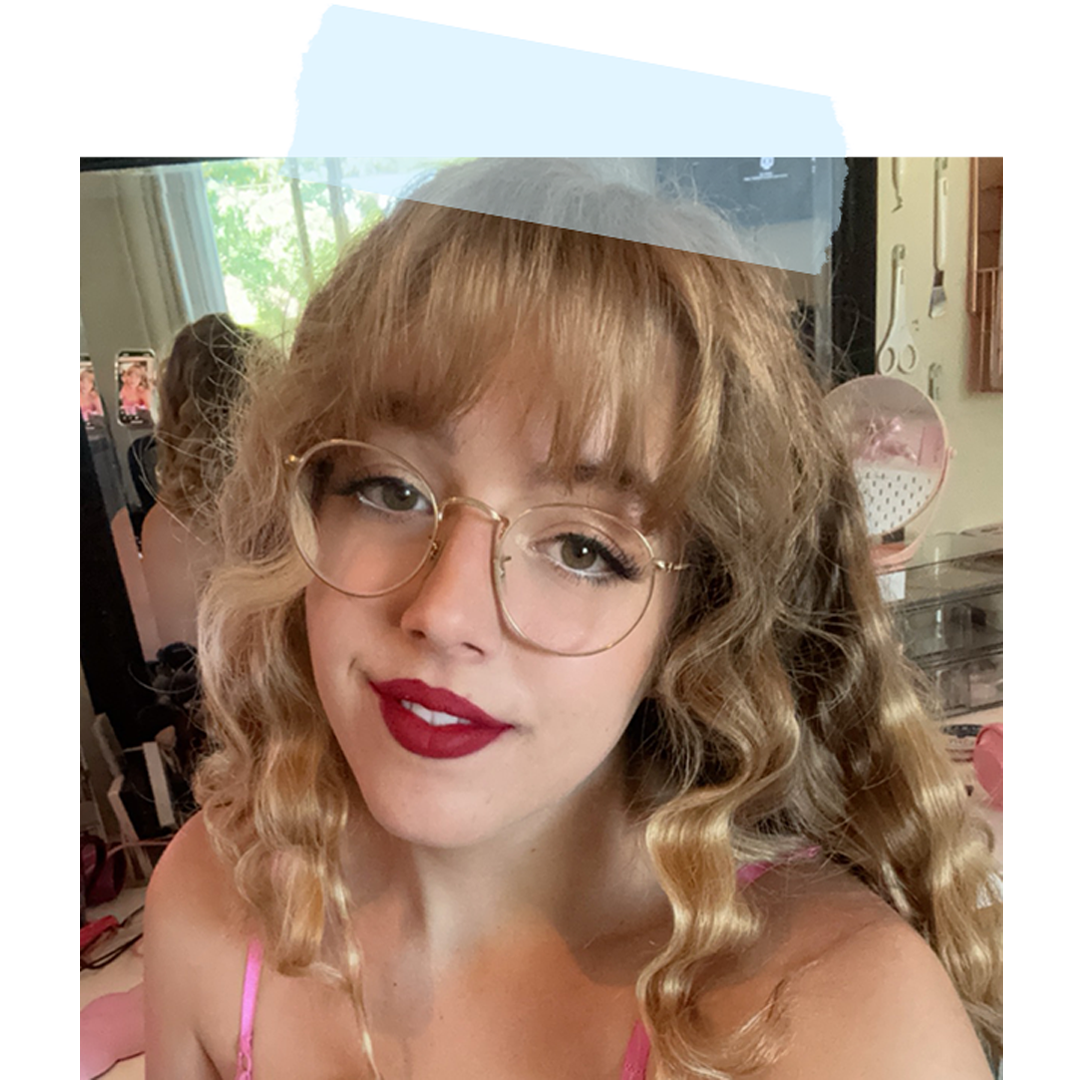 photo of a woman with blonde hair, gold glass, bangs, and red lipstick on, smiling into the camera.