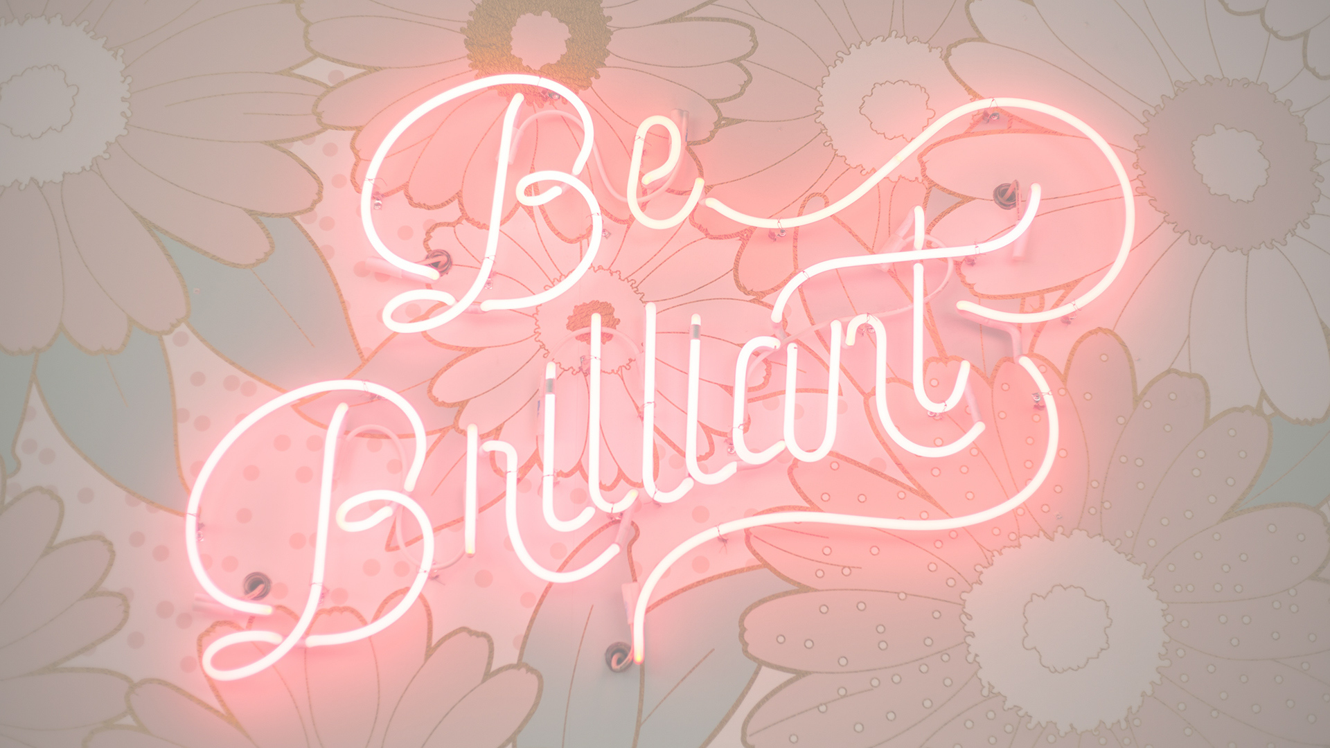 this is a neon sign saying be brilliant against a floral backdrop