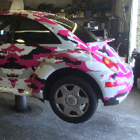 pink, gray, and white camo detailed new volkswagen bug sitting slight up on a lift in the shop