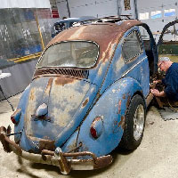 old rusty and beautifully patinaed volkswagen bug with mechanic paying close attention to the side wall trim