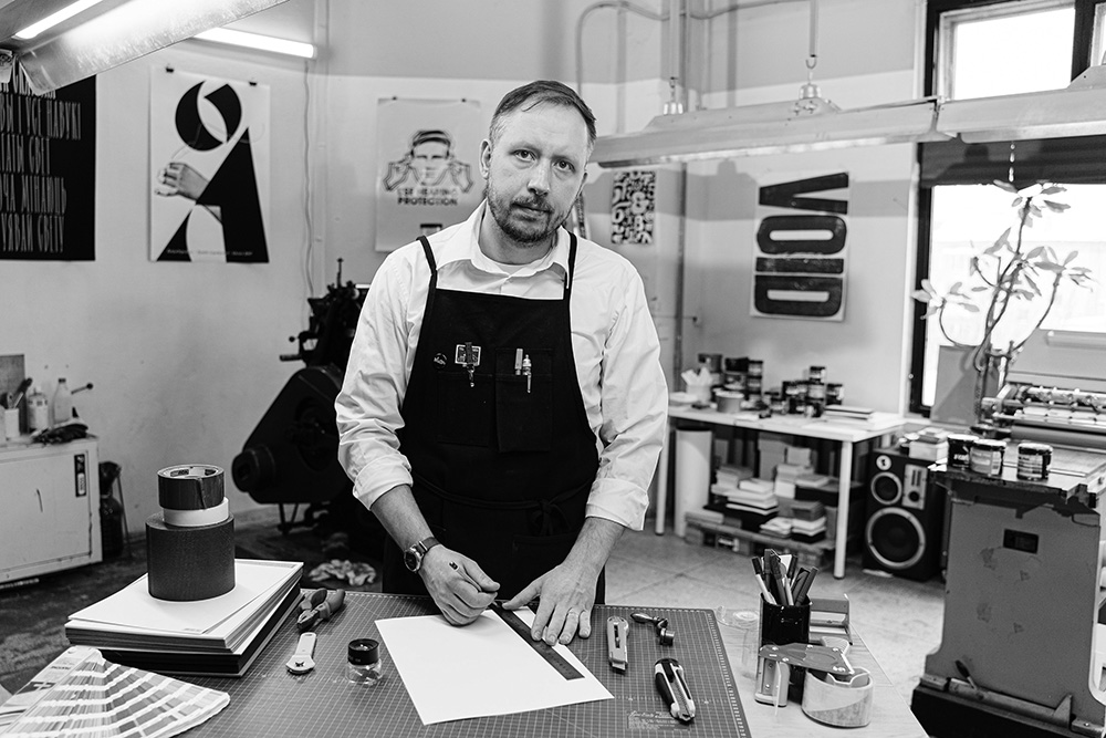 man at his workshop desk looking at different paint while looking at the camera with a serious straight face