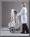 a woman stands as she is tilting xray equiptment on its wheels, demonstrating the ability to roll portable xray equiptment.